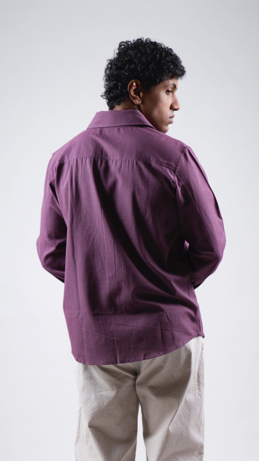 Person wearing a purple shirt and beige pants on a white background