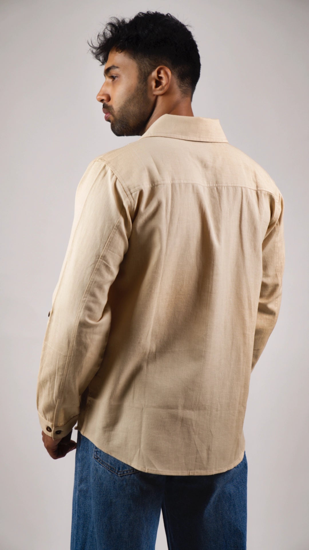 Back view of a model wearing a beige shirt and blue jeans against a plain background