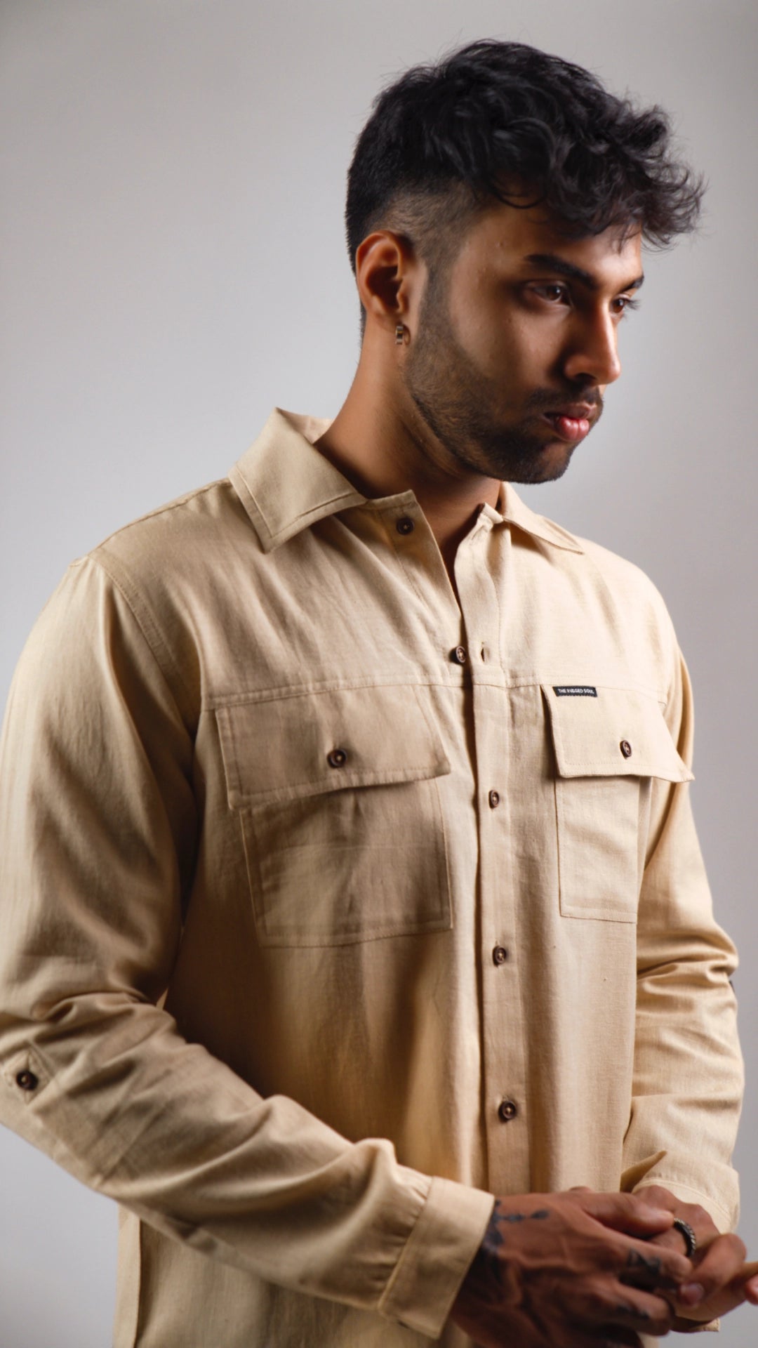 closeup of a man wearing a beige shirt against a gray background
