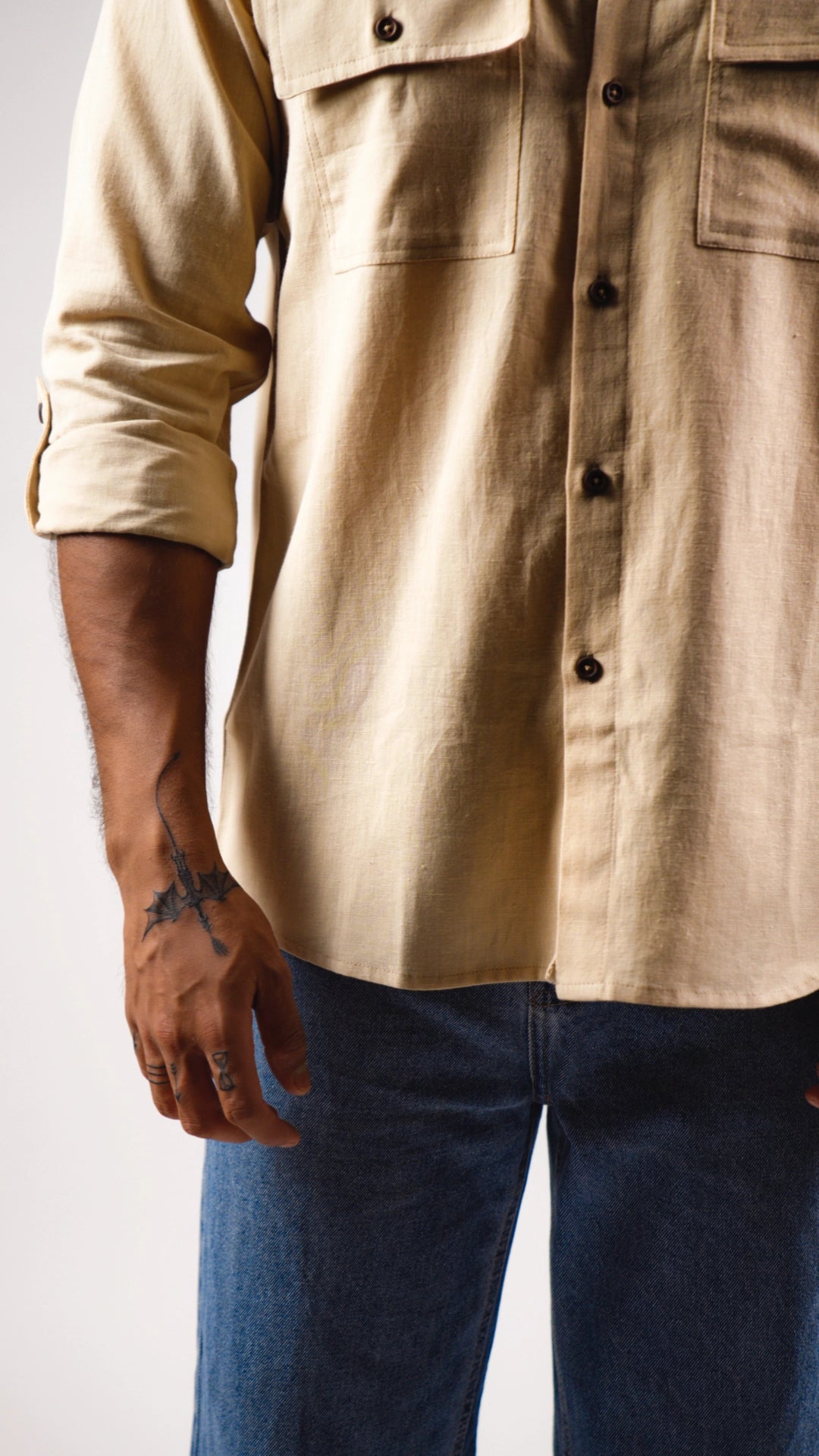 Beige shirt with rolled-up sleeves worn by a person on a plain background