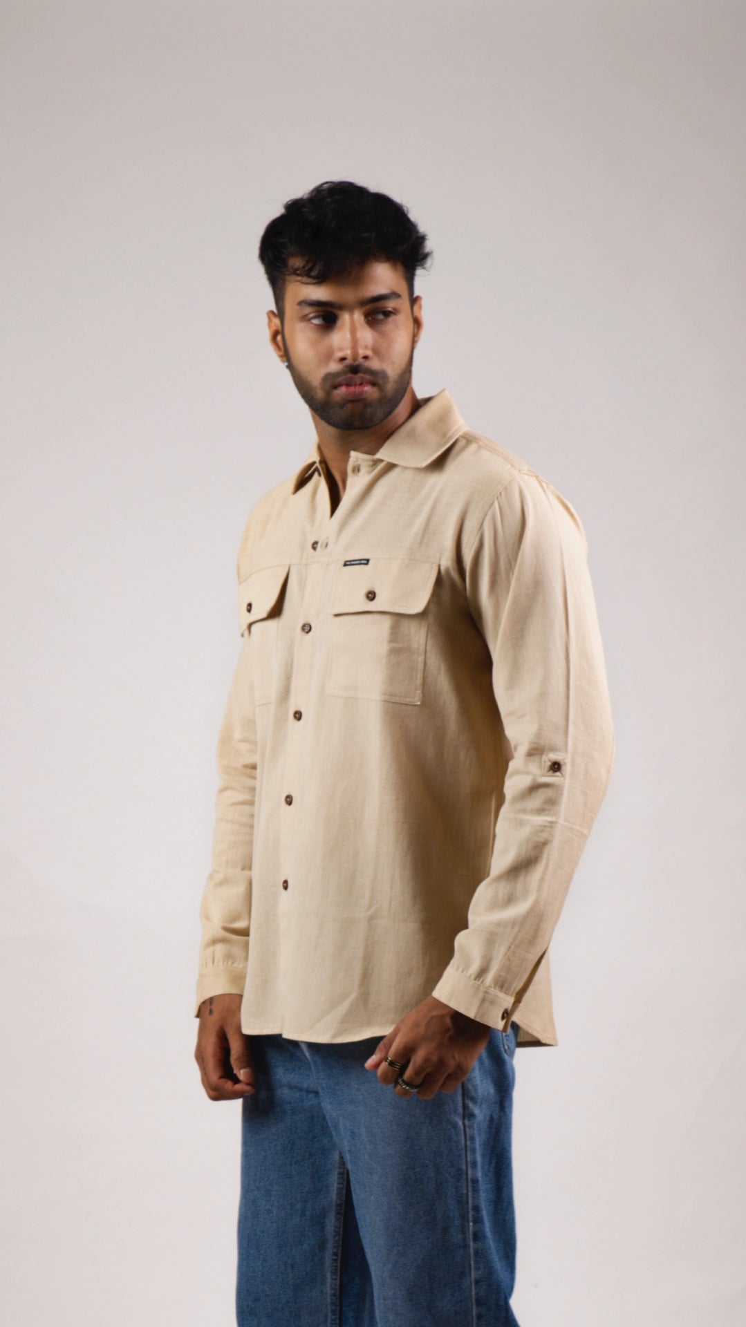 Man wearing a beige shirt with button details on a plain background