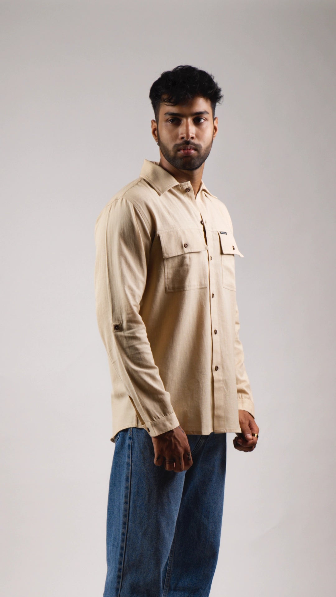 Model wearing a beige shirt and blue jeans against a gray background