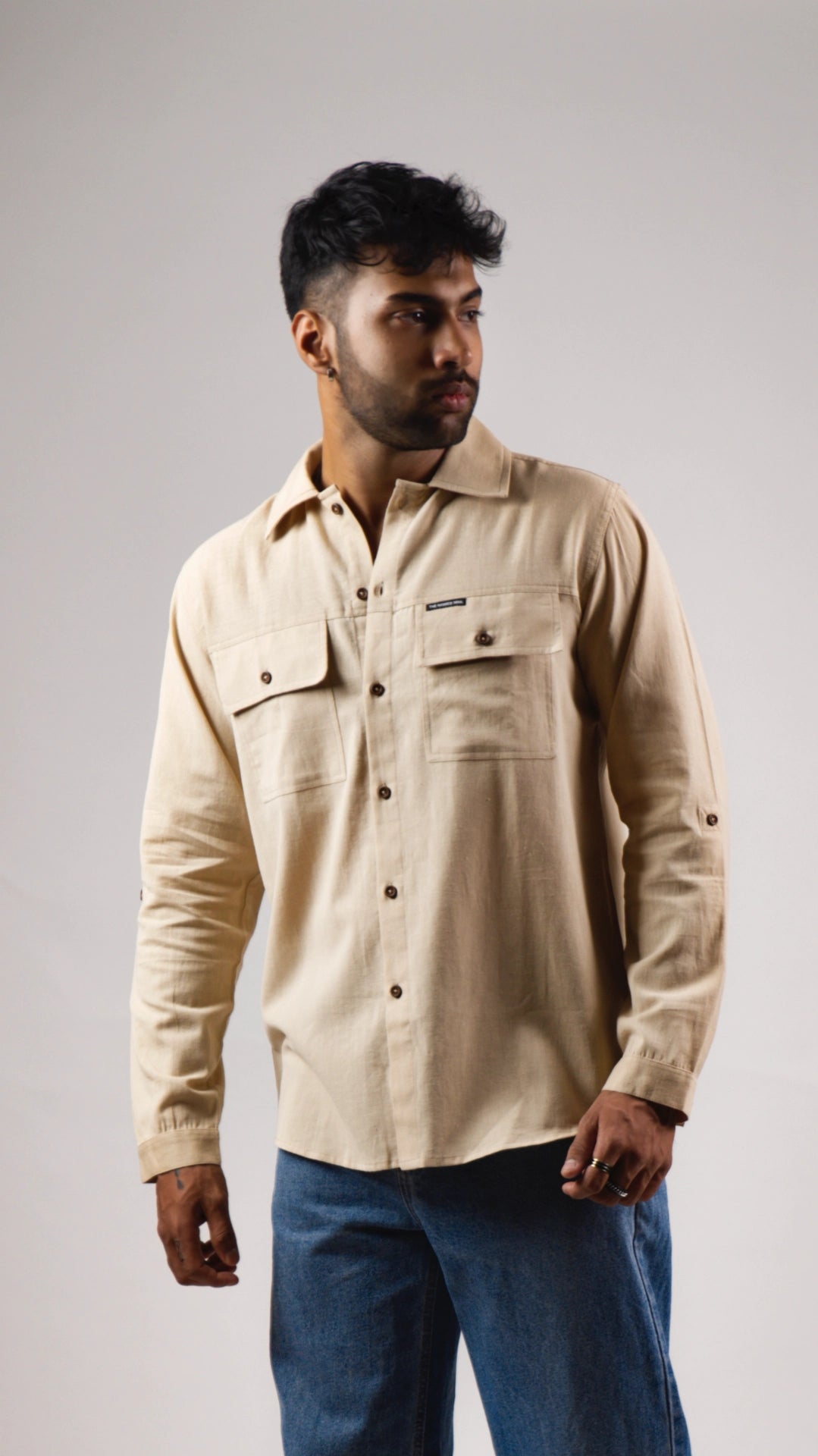 Man wearing a beige shirt with two front pockets on a plain background