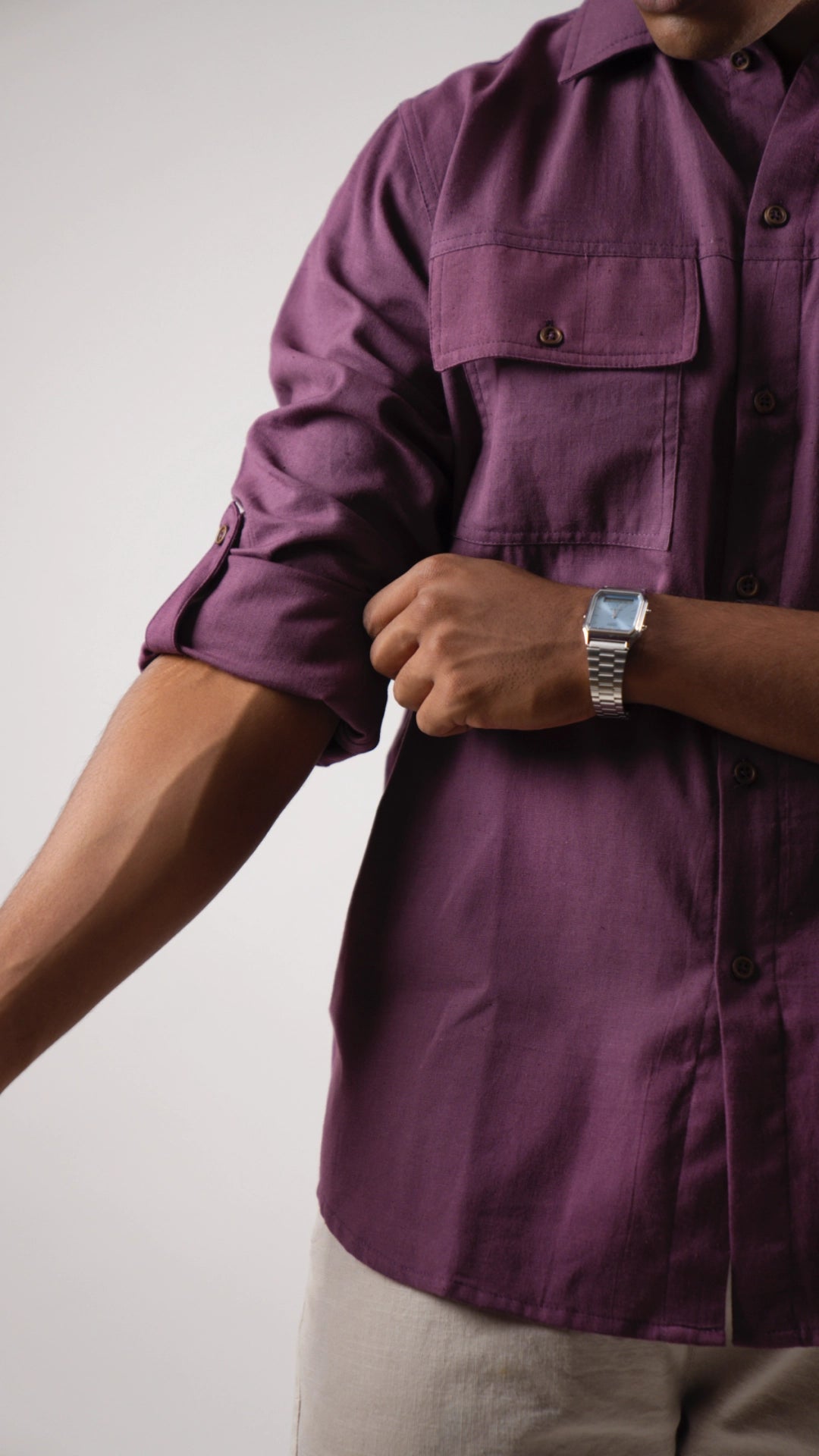 Person wearing a purple shirt with rolled-up sleeves on a plain background