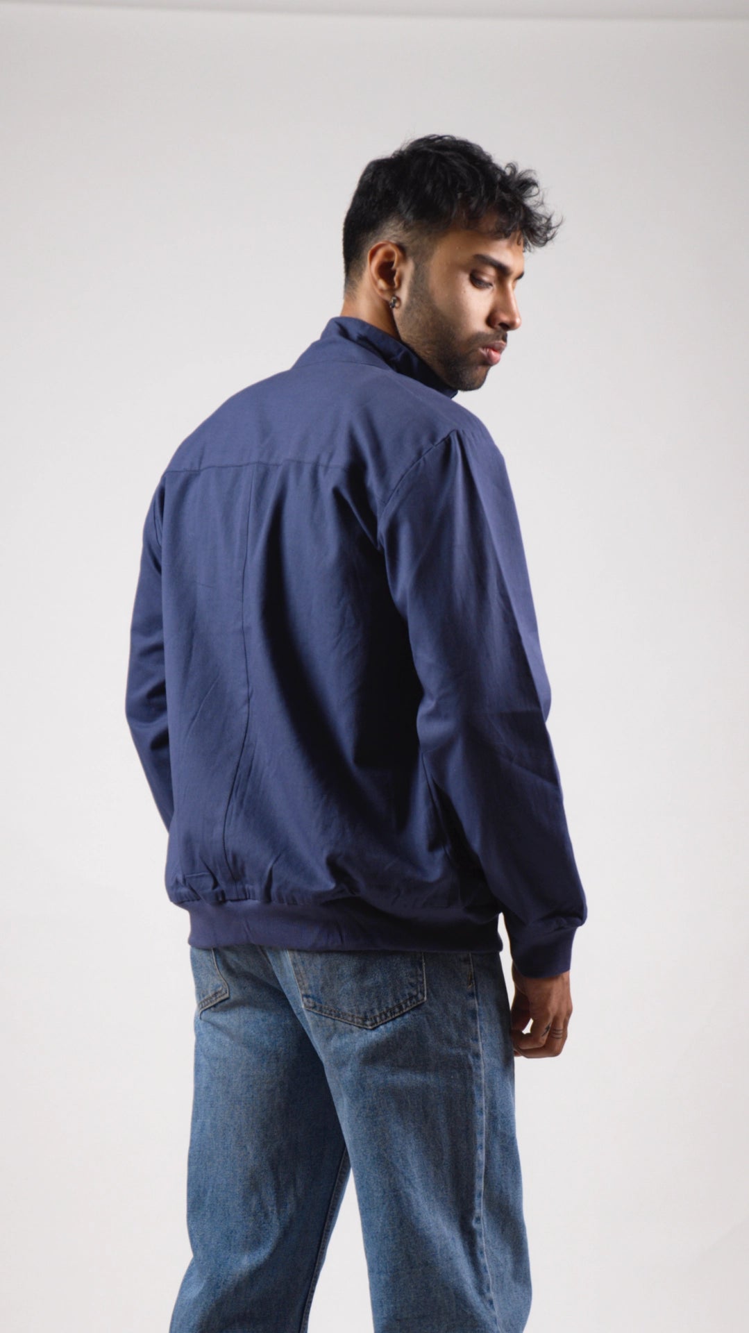 Back view of a man wearing a blue jacket and jeans on a white background
