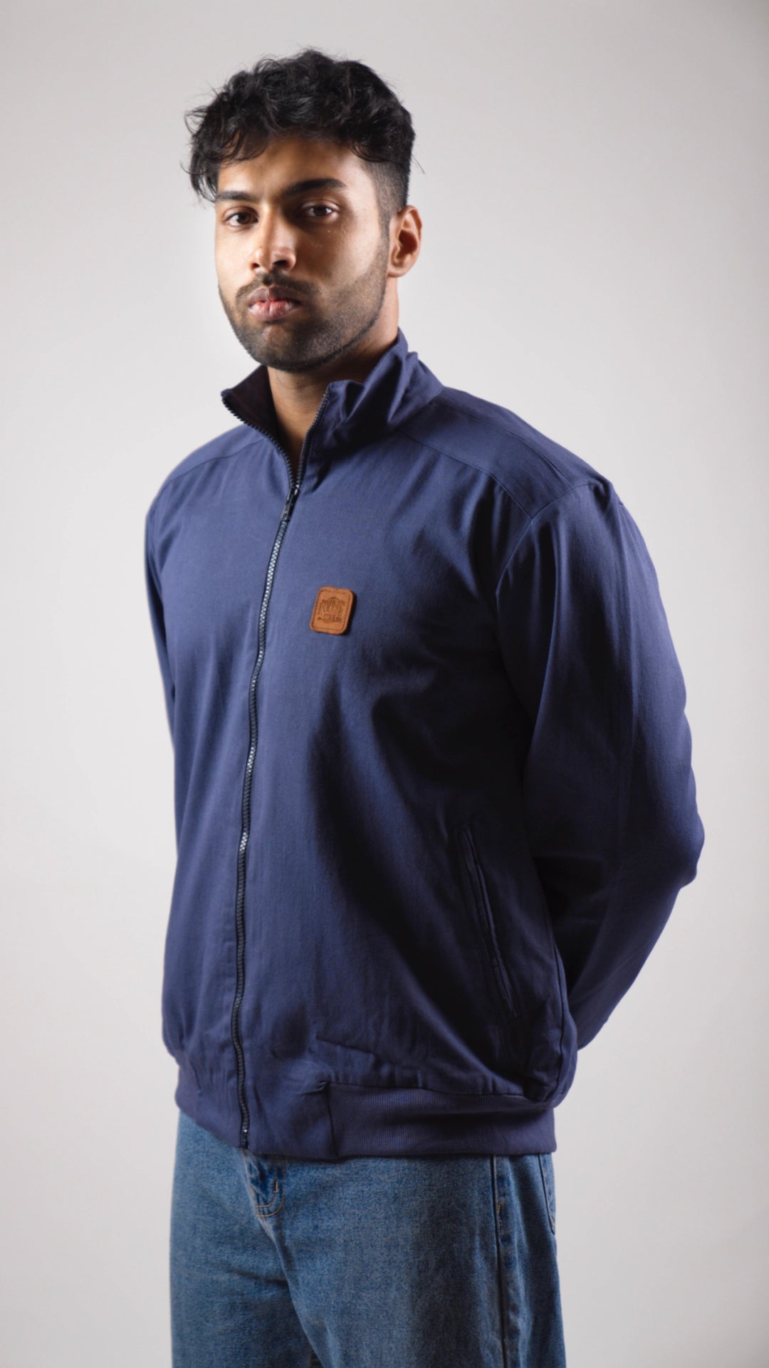 Man wearing a blue jacket with a logo on a plain background