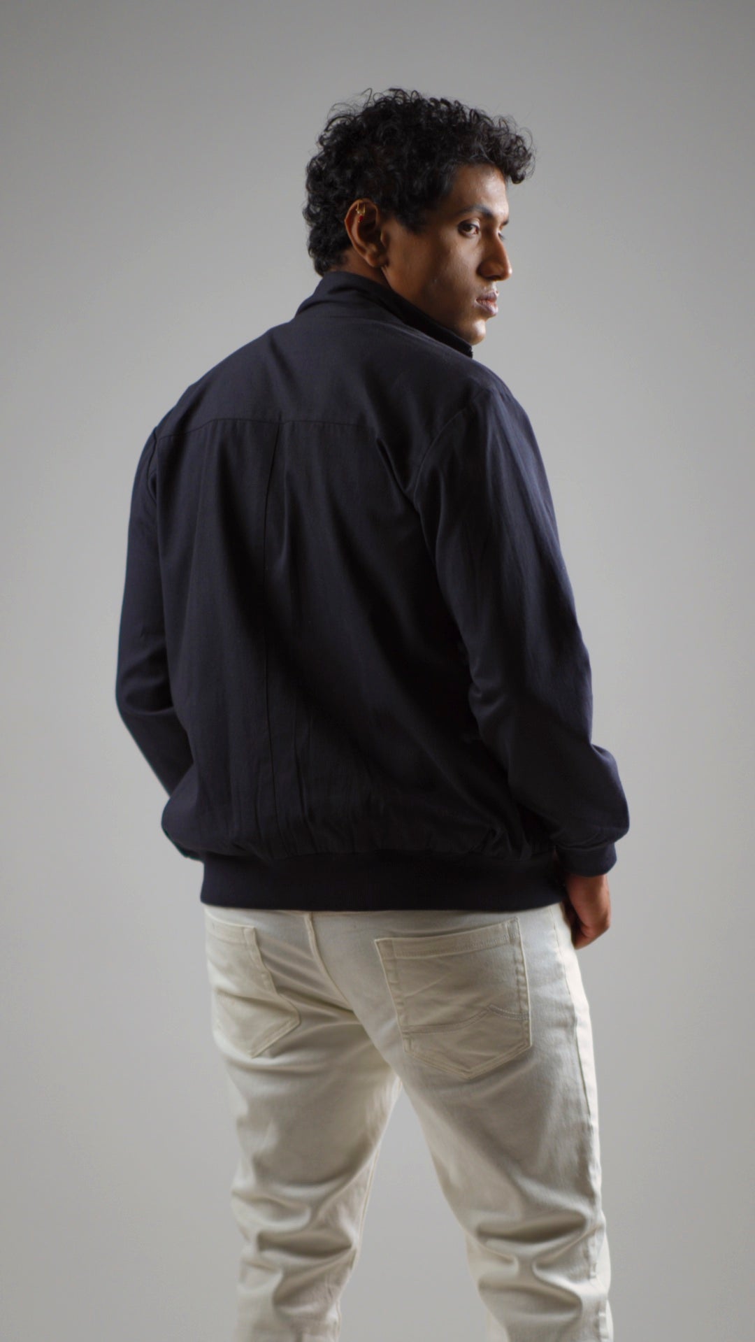 Back view of a man wearing a midnight navy cotton twill jacket on a light coloured pant and shirt