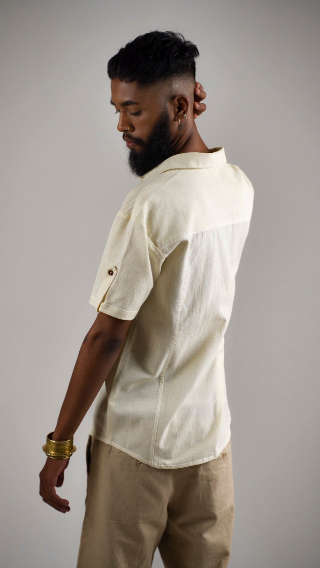 Back view of a man posing in an alabaster white cotton linen shirt with contrast stitching and patch pockets