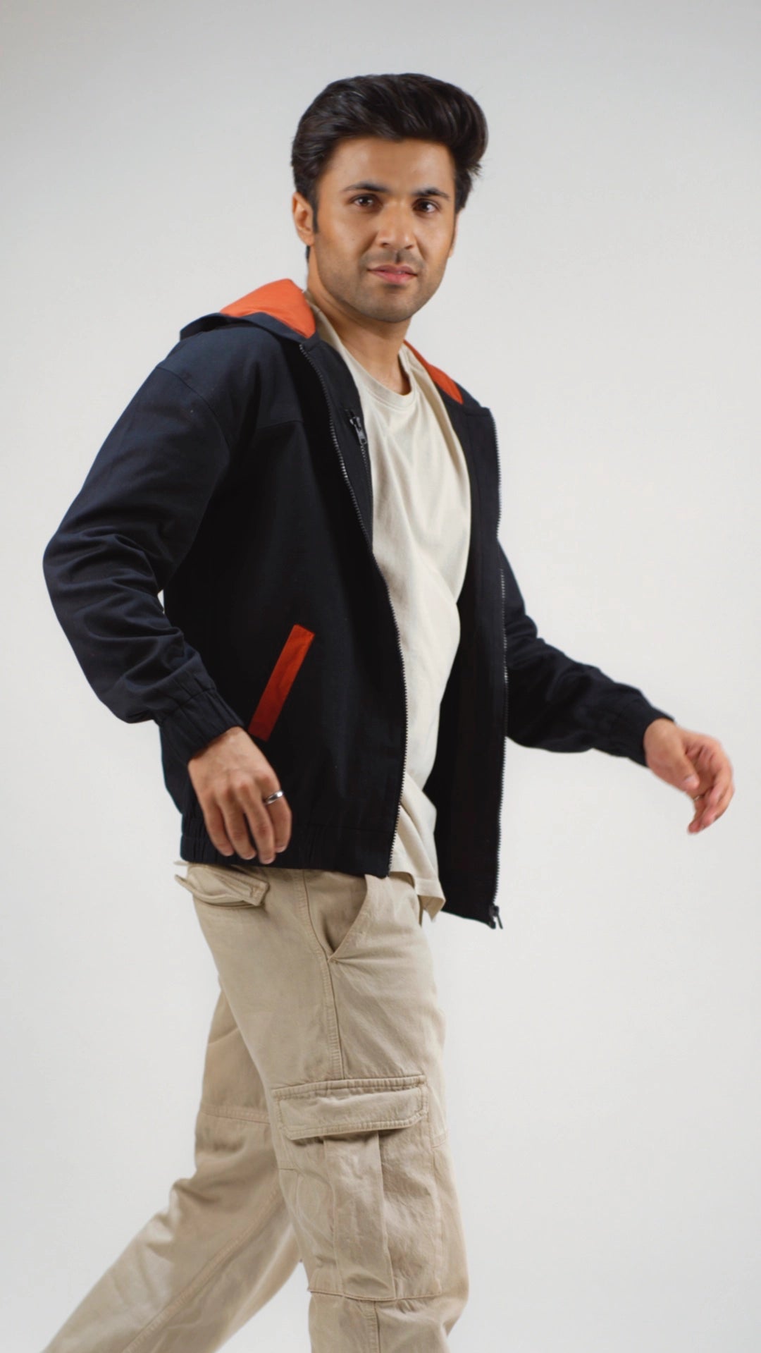 Man wearing a black hoodie with rust accents and beige pants on a white background