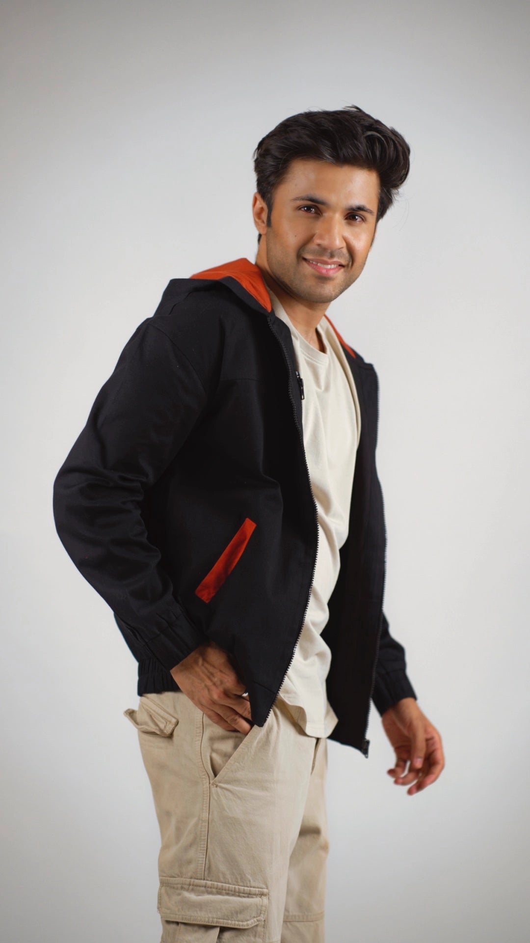 Man wearing a black hoodie with rust accents and beige pants on a white background