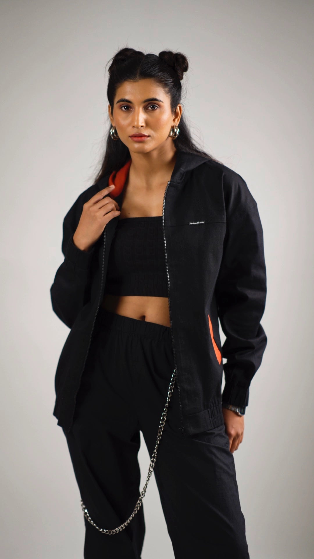 Woman wearing a black cotton hoodie with rust accents with a gray background