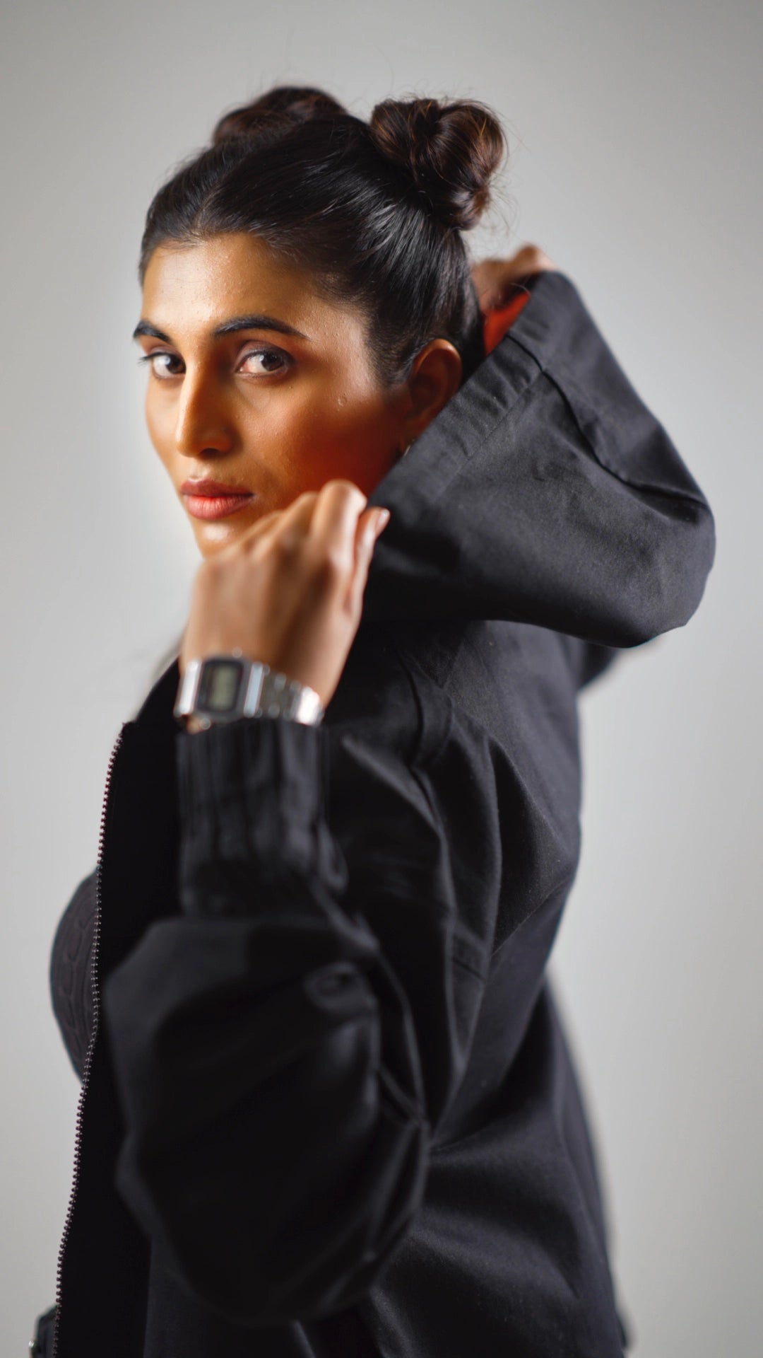 Sideways closeup of a woman wearing a black hoodie with rust accents against a gray background