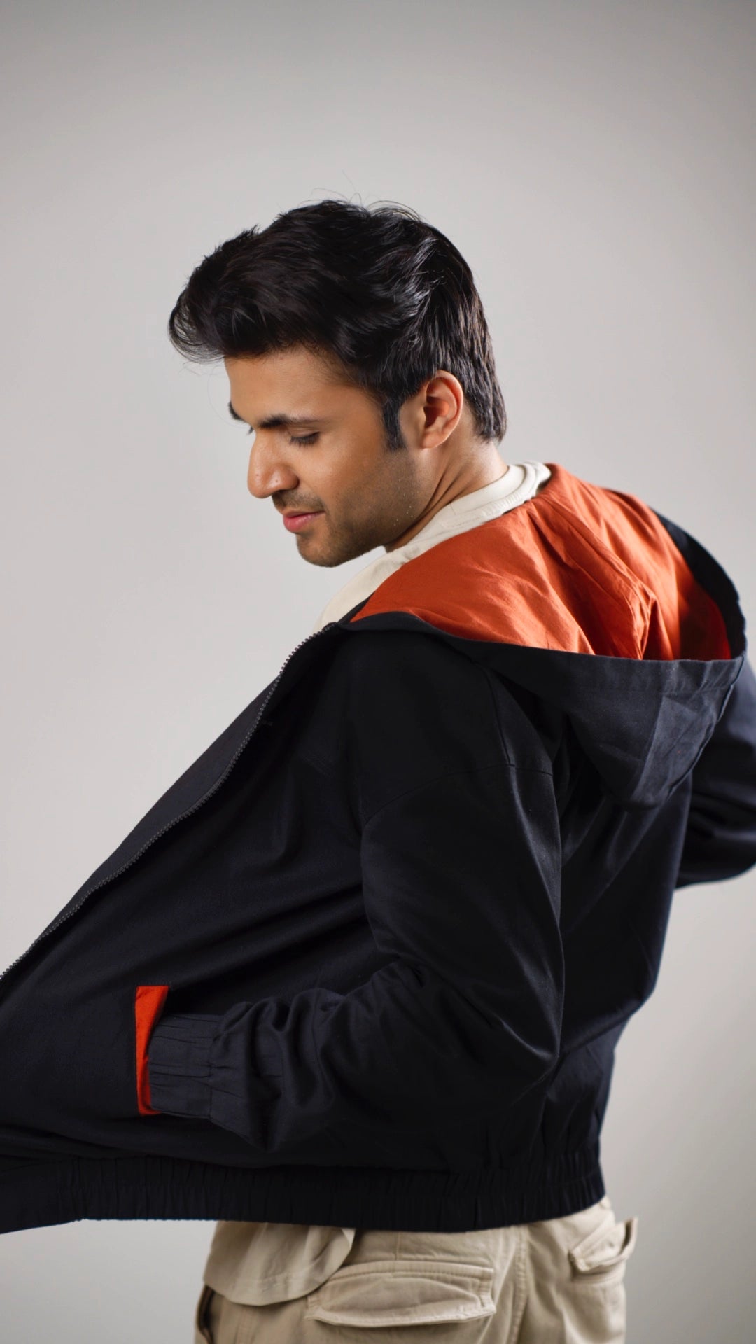 Back view of a man wearing a black hoodie with rust accents on a plain background