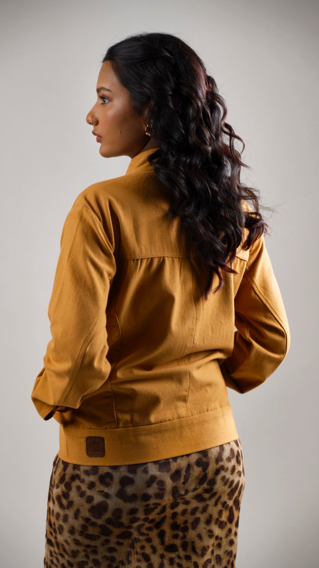 Back view of a woman wearing a mustard coloured cotton canvas jacket over a leopard print