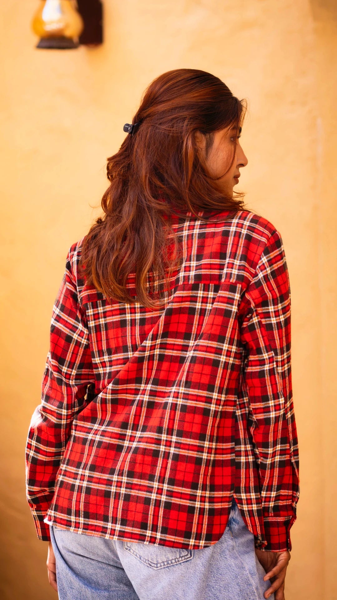 Woman wearing a red and black plaid shirt against a beige wall