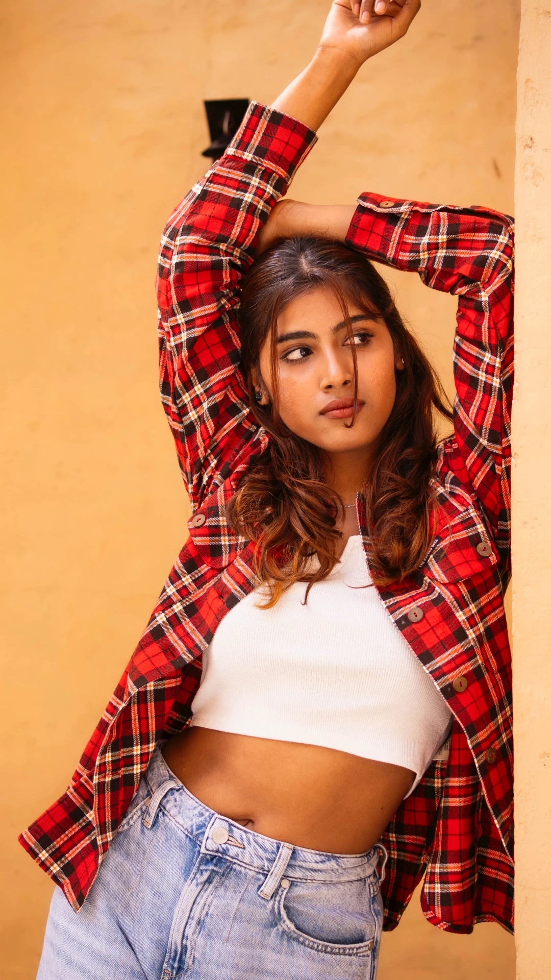 Woman wearing a red plaid shirt over a white top and blue jeans against a beige background