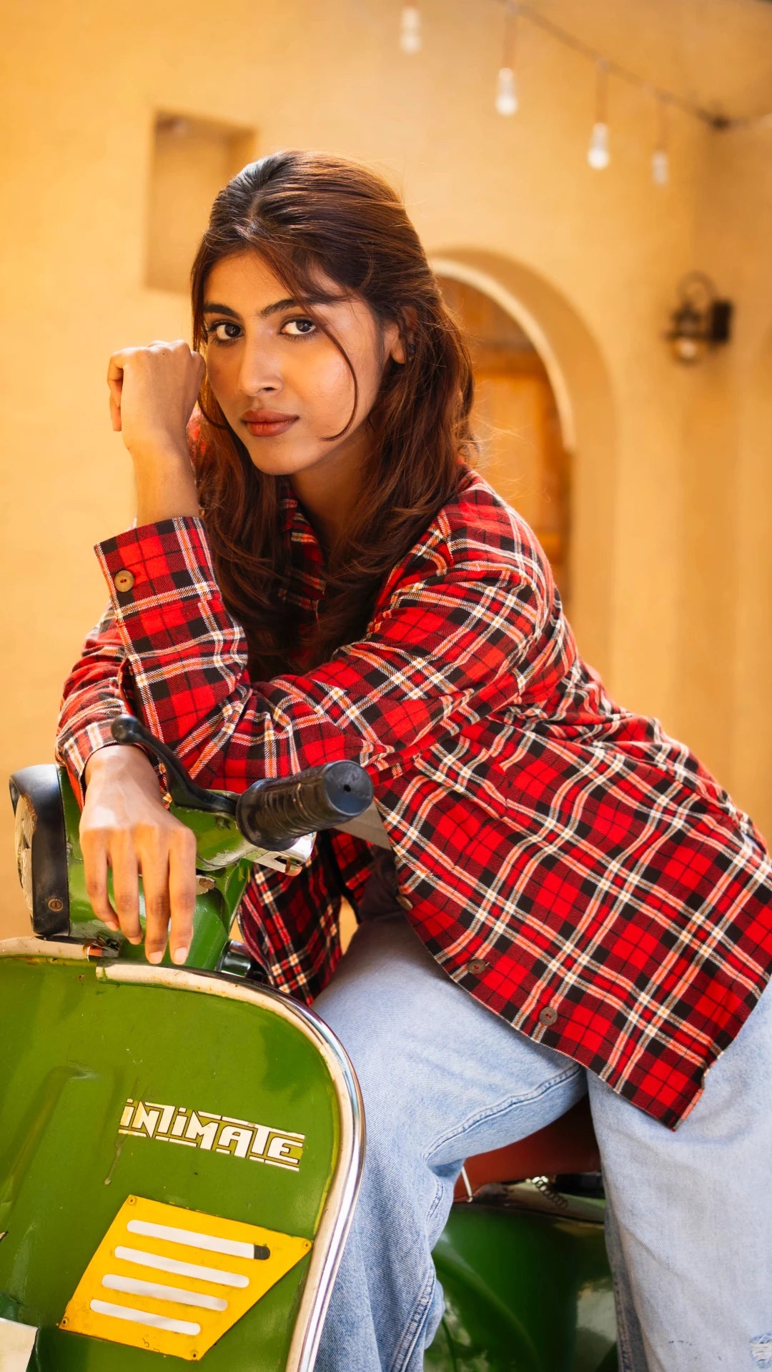 Woman in a red plaid shirt sitting on a green scooter with a blurred background