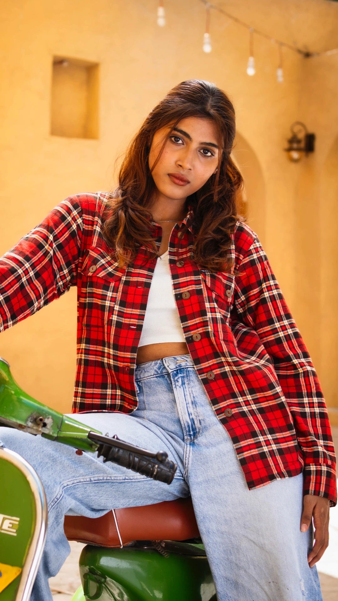 Woman wearing a red plaid shirt and blue jeans sitting on a green motorcycle.