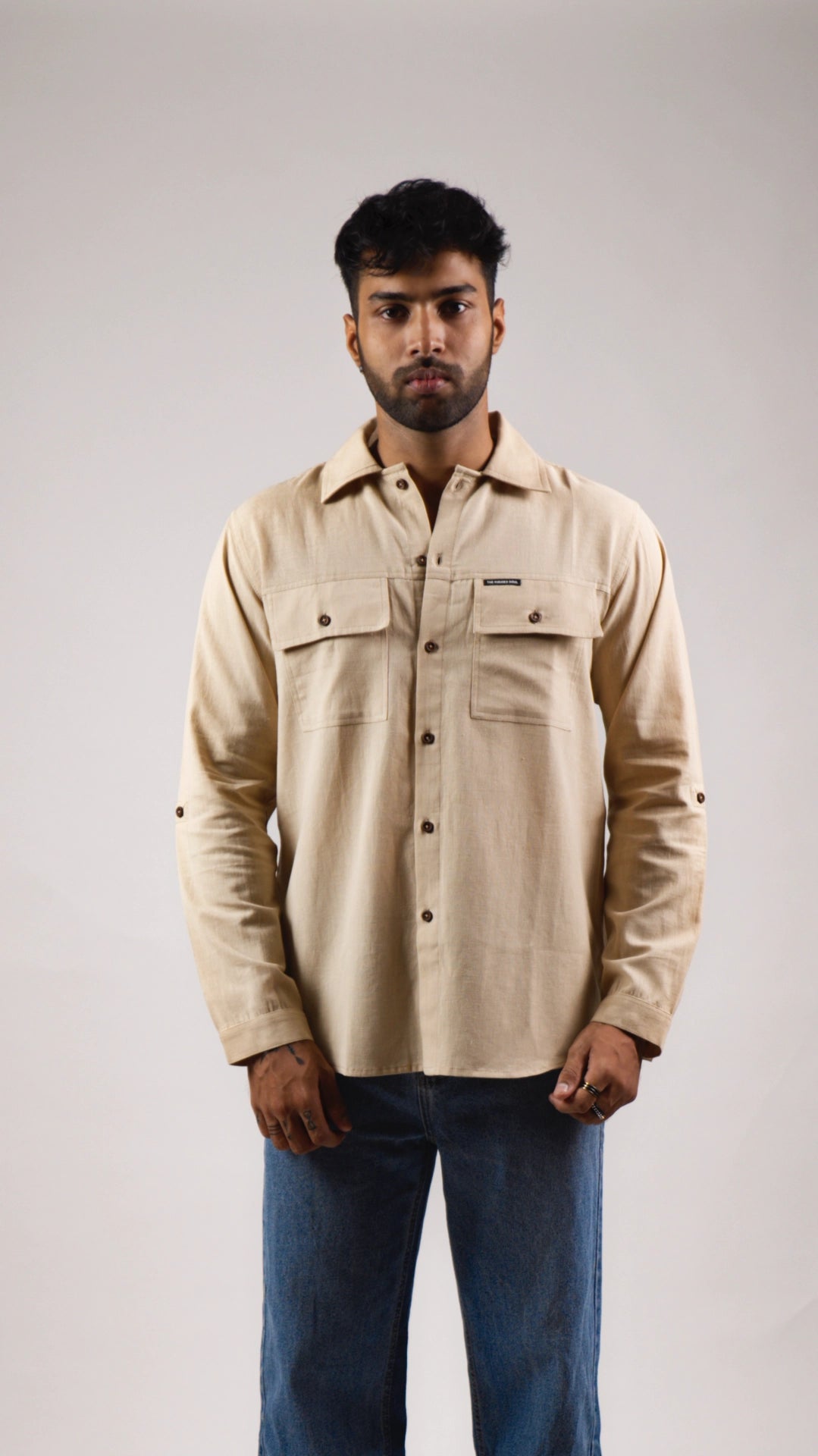 Man wearing a beige shirt with a brand logo on a plain background