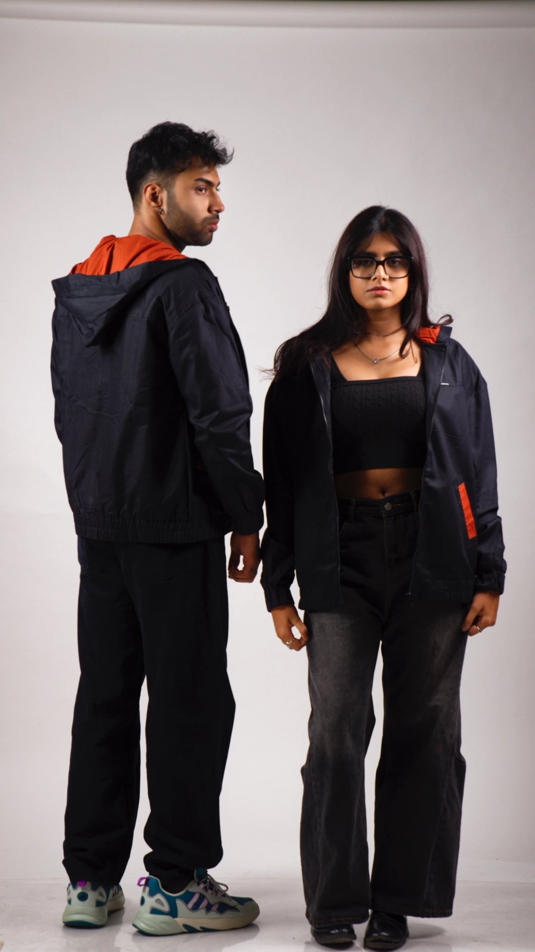 Male and female models wearing matching black cotton hoodies with rust accents on a white background