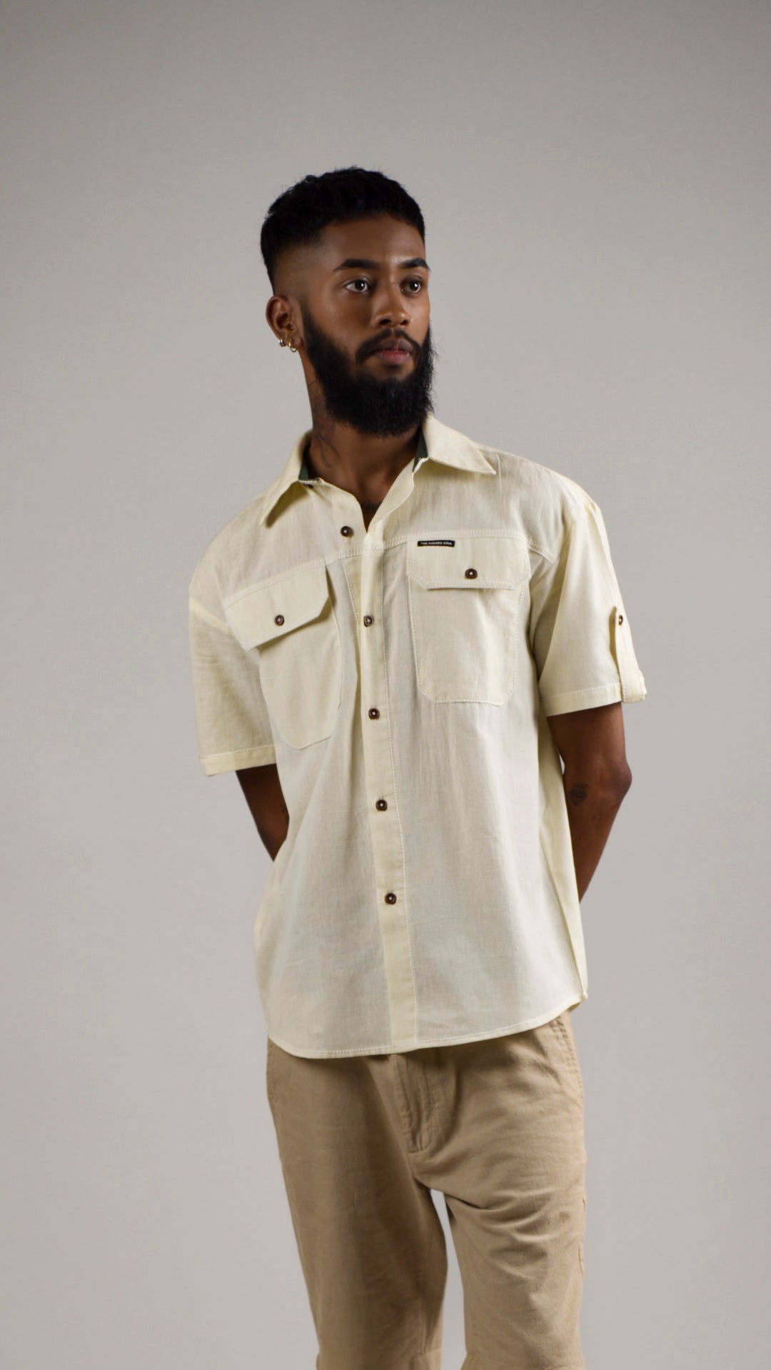 A man wearing a short-sleeved, alabaster white cotton linen shirt with patch pockets and contrast stitching.