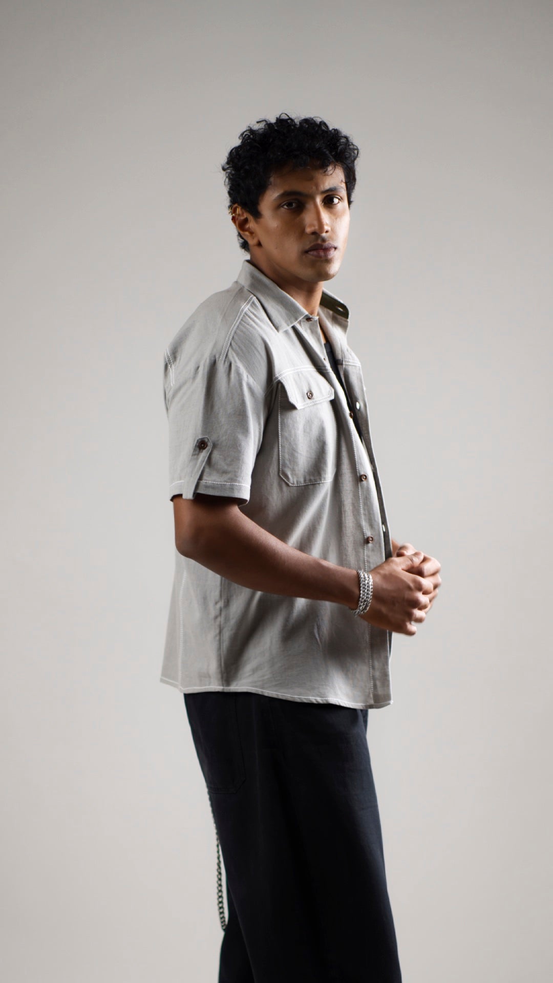 A man standing in a casual pose wearing a slate grey, half-sleeve, button-up cotton linen shirt with patch pockets.