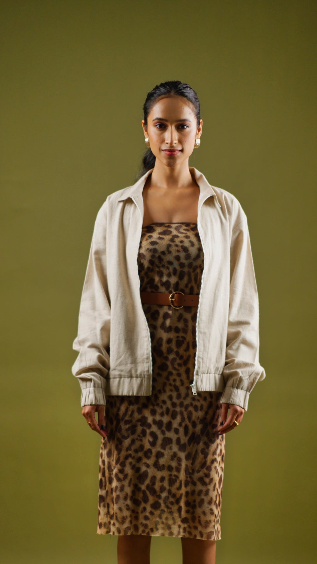 A woman wearing a beige hemp bomber jacket over a leopard print dress, standing against a green background.