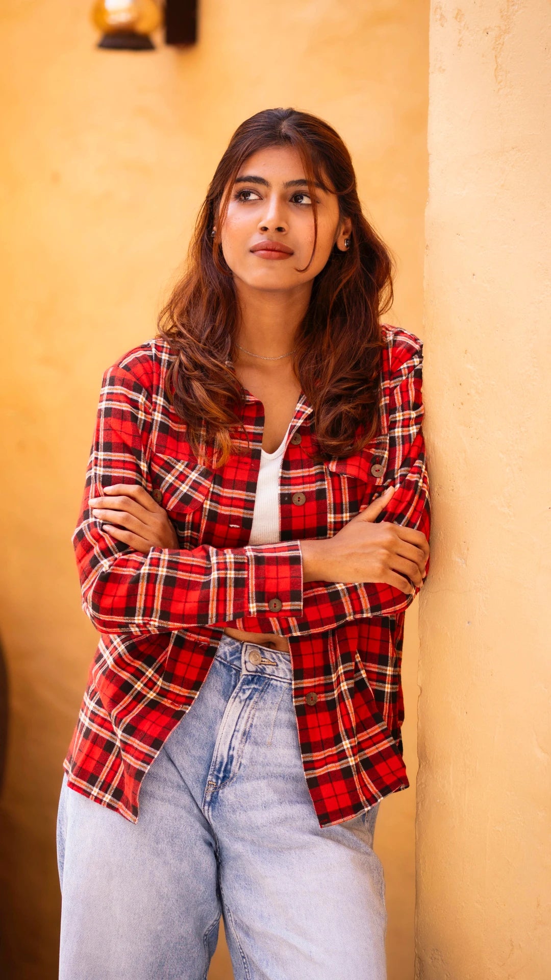 Woman wearing a red plaid shirt and light blue jeans against a beige wall.
