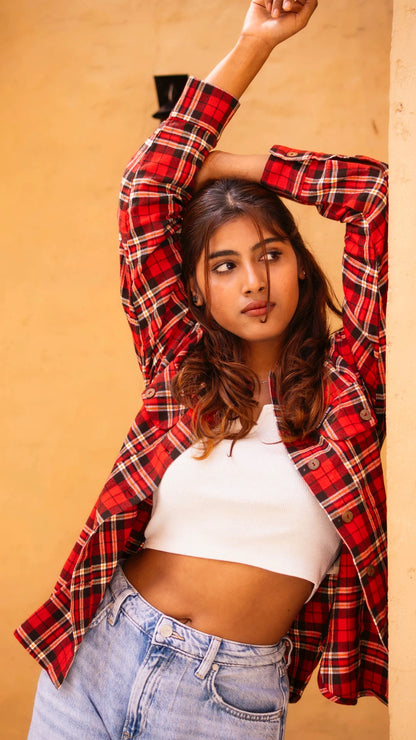 Woman wearing a red plaid shirt over a white top and blue jeans against a beige background