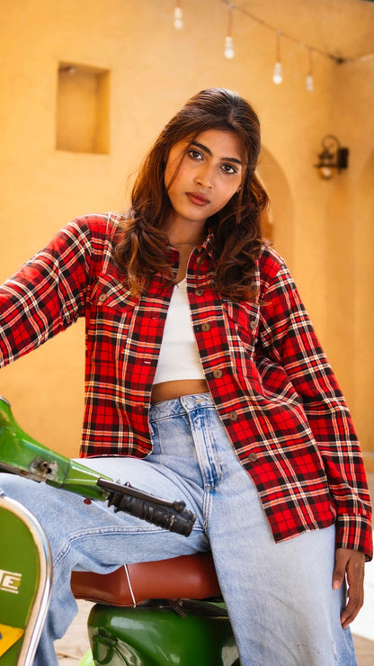 Woman wearing a red plaid shirt and blue jeans sitting on a green motorcycle.
